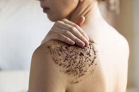 A woman using a coffee scrub on her back