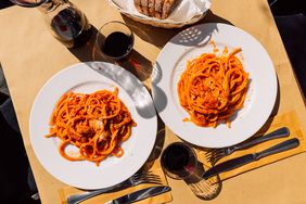 Two plates of Pasta with glasses of red wine