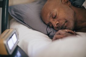 Retired man sleeping by alarm clock
