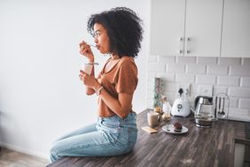 Woman sitting on the counter eating yogurt. Getty Images.