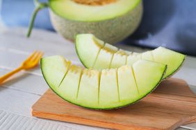 Two slices of honeydew melon on a wooden cutting board with a half slice melon behind it. 