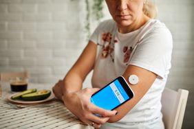Mature woman swiping continuous glucose monitor with smart phone application.