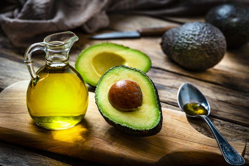 Avocados and avocado oil on a wooden table with a spoon of oil