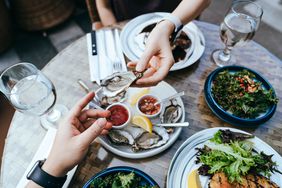 two people passing an oyster at a table outdoors. 