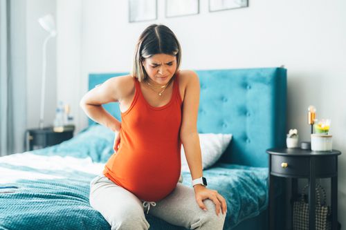 Pregnant woman with kidney infection feeling pain while sitting on bed