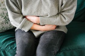 woman in gray sweater holding stomach uteren pain