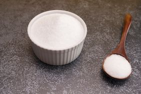 A white ceramic bowl filled with Erythritol sugar substitute. There is a wooden spoon also filled with erythritol. 