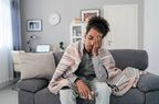 young man sitting on couch with blanket experiencing head pain