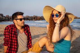 Young redheaded girl with a hat and sunglasses spends the afternoon with a brown boy on a Mediterranean beach. 