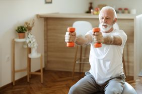An older man lifts dumbbells in front of him as he sits on an exercise ball