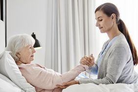 A healthcare provider assists an older woman lying in a bed