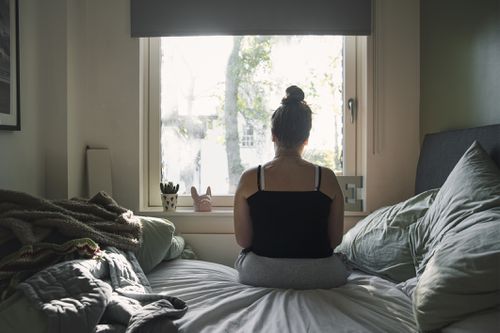 woman looking out window from bed