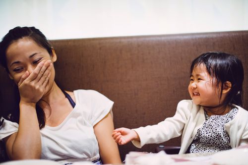 A woman covers her mouth with her hand as the child next to her laughs