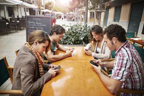 Four friends all looking at their phones at cafe 