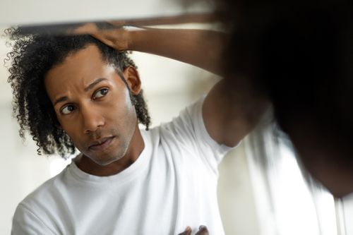 A man checks his curly hair in the mirror for signs of alopecia