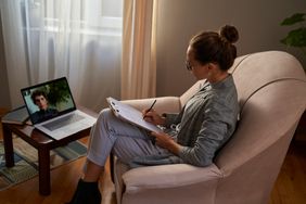 Woman takes notes during an online therapy session