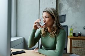 A woman drinking a glass of water while sitting at her desk