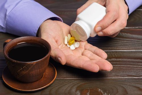 Male hands pouring medications and vitamins into his hands, with a cup of coffee next to him