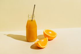 Colorful bottle of freshly squeezed orange juice with fresh ingredients oranges on beige background.
