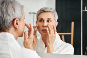 An older woman applying retinol cream while looking in the mirror