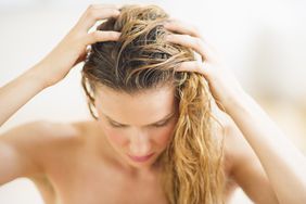 A blonde woman with wet hair touching her scalp