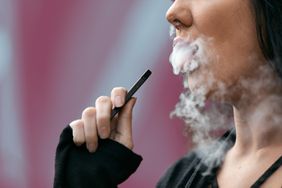 vaping-higher-covid-risk , Woman outdoors using an electronic cigarette to "vape".