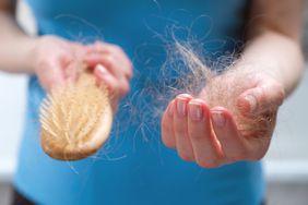 A woman holding a wooden comb in her hands, and a clump of hair that is falling out on the other hand