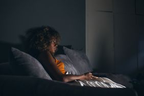 Woman sitting on a couch at night watching TV in low light